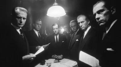 black and white film noir photograph, group of seven professionals standing around a small table in a dark room, each ho